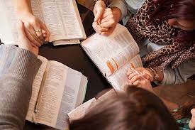 multiple people around a table with their bibles open for study