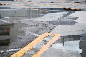 a close up of a parking lot with drainage problems and broken pavement