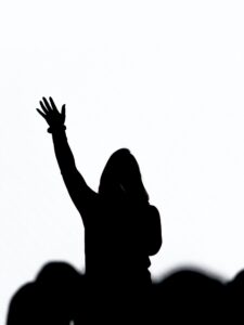 A silhouette of a singer with her right hand raised in worship